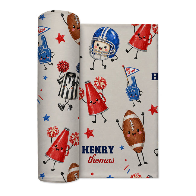 A roll of personalized baby swaddle blanket. The blanket has a light beige background with a sports-themed cartoon pattern featuring a football, referee, cheerleader foam fingers, pom-poms, stars, and the text 'HENRY Thomas'.