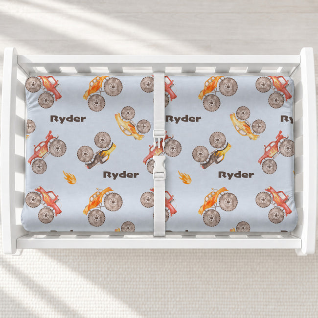 Monster Trucks changing pad cover personalized with Ryder, featuring colorful watercolor trucks on pale blue in a white changing table.