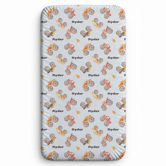 Monster Trucks personalized twin sheet featuring brown Ryder lettering, watercolor monster trucks, oversized tires, and orange flame accents on pale blue.