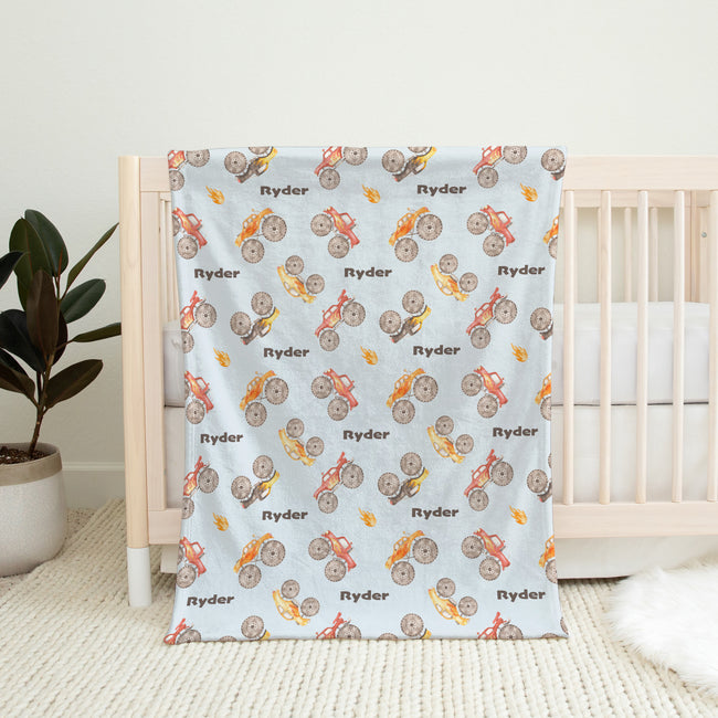 Monster Trucks baby blanket personalized with Ryder, draped over a wooden crib in a bright nursery.