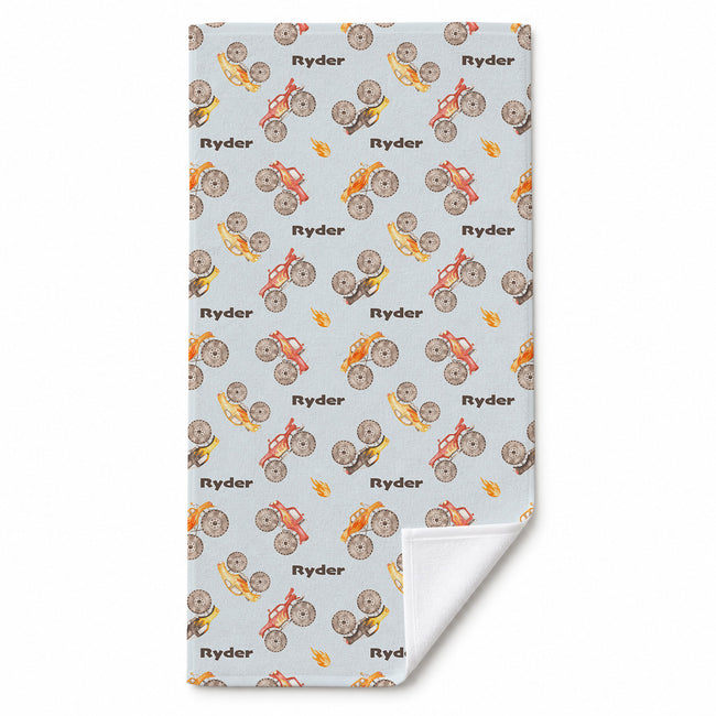 Monster Trucks beach towel personalized with Ryder, featuring watercolor trucks and flames on pale blue, with a corner folded to show the white reverse.