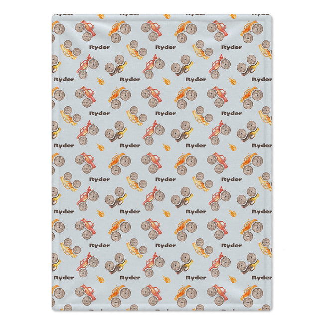 Full view of the Monster Trucks personalized blanket with repeating brown Ryder lettering and watercolor trucks on pale blue.