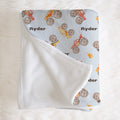 Folded Monster Trucks blanket with Ryder lettering and watercolor trucks, with a corner turned back to reveal the white reverse.