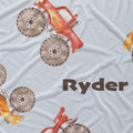 Close-up of brown Ryder lettering beside red and yellow watercolor monster trucks on pale blue fabric.