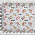 Close-up of the Monster Trucks crib sheet showing watercolor trucks, oversized tires, orange flames, and brown Ryder lettering.
