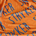 Close-up of an orange plush fabric with blue text reading 'STRYKER' repeated across the surface.