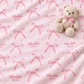 A plush light pink blanket with an all-over repeating pattern of pink bows and the custom text 'Charlotte MAE' in pink, styled with a small beige teddy bear wearing a matching pink bow on a soft white background.