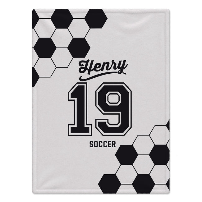 A white custom blanket featuring a black and white soccer theme. The design includes a classic black and white hexagonal soccer ball pattern in the top-left and bottom-right corners, with the text 'Henry', '19', and 'SOCCER' printed in black in the center.