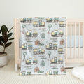 A personalized baby blanket with a vintage train pattern and the name 'HENRY william' printed on it, draped over a light wood crib in a nursery setting.