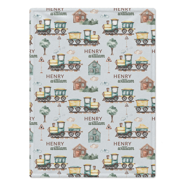 A personalized baby blanket featuring a repeating pattern of vintage toy trains, small houses, trees, and the text 'HENRY william' on a light gray background.