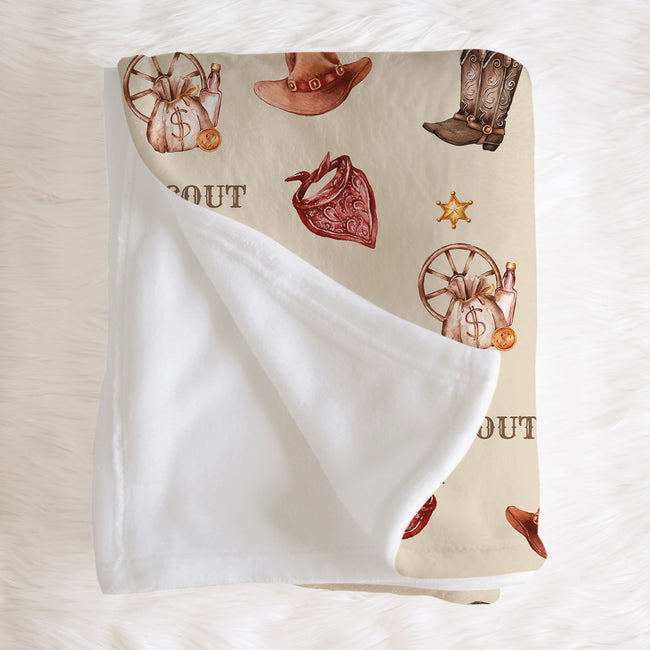 A folded fleece blanket with a western-themed print on one side and a soft white sherpa lining on the reverse, displayed on a white faux fur background.