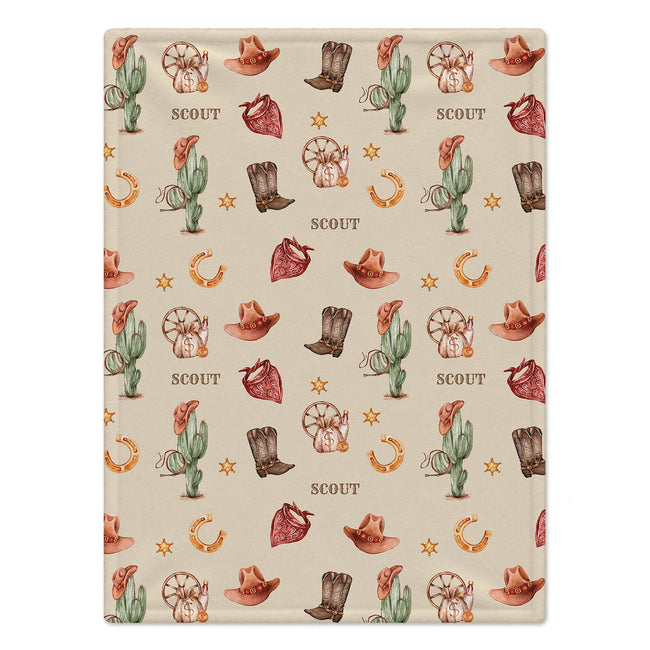 A rectangular blanket with a western-themed pattern featuring cacti, cowboy hats, boots, horseshoes, stars, and the word 'SCOUT' repeated on a warm beige background.