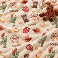 A plush fleece blanket with a western 'SCOUT' theme, featuring a brown plush toy horse on the right side. The blanket has a cream-colored background with a repeating pattern of brown cowboy hats, green cacti, red bandanas, brown boots, gold horseshoes, and brown wagon wheels, with the word 'SCOUT' printed in brown text.