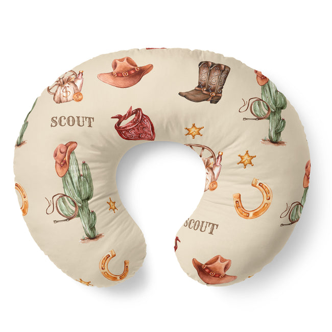 A U-shaped nursing pillow with a western-themed print featuring cacti, cowboy hats, boots, horseshoes, stars, and the word 'SCOUT' on a cream background.