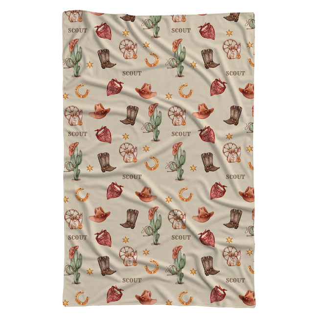 Full view of a Wild West swaddle blanket with Scout repeated among watercolor cowboy boots, hats, cacti and bandanas.