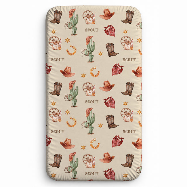 Wild West twin fitted sheet personalized with Scout, shown on a mattress with watercolor cowboy boots, hats, cacti and bandanas.