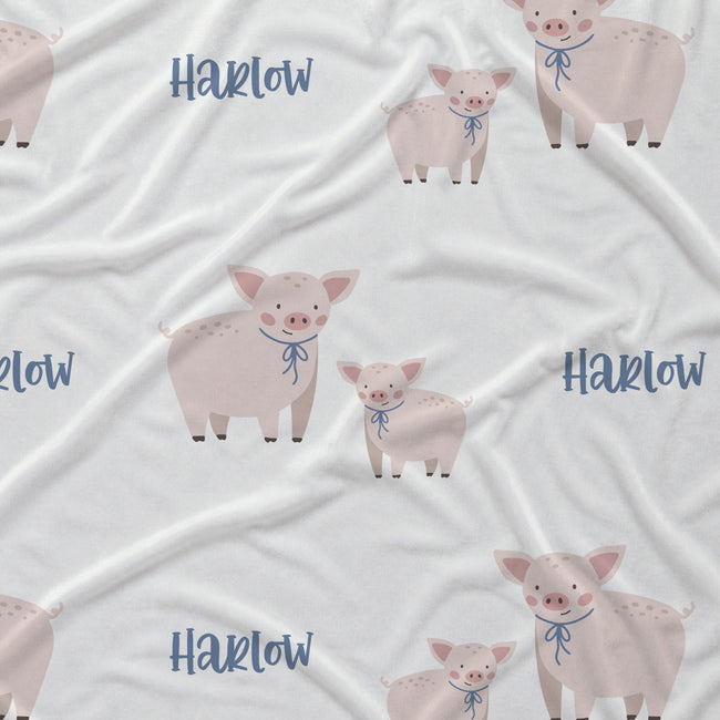 White fabric with a repeating pattern of cartoon pigs and the word 'Harlow' in blue script.