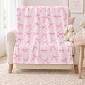 Personalized blush pink bow blanket with the repeated name Charlotte Mae draped over an ivory nursery chair beside a plush bunny.
