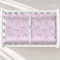 Personalized blush pink changing pad cover with watercolor bows, tiny sparkles, and the name Charlotte Mae on a white changing table.