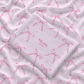 Folded blush pink personalized swaddle blanket with watercolor bows, tiny sparkles, and the name Charlotte Mae.