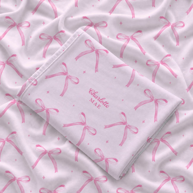 Folded blush pink personalized swaddle blanket with watercolor bows, tiny sparkles, and the name Charlotte Mae.