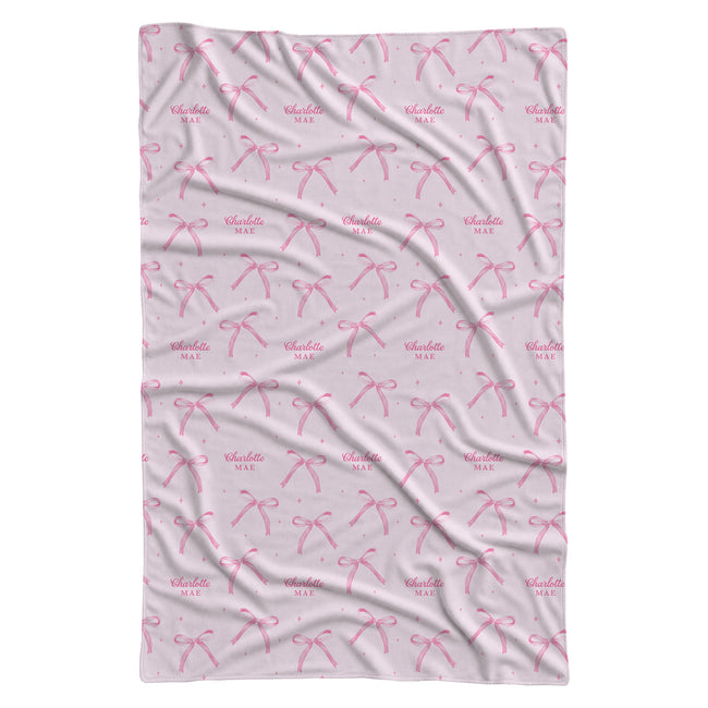 Blush pink personalized swaddle blanket with watercolor bows, tiny sparkles, and the name Charlotte Mae.