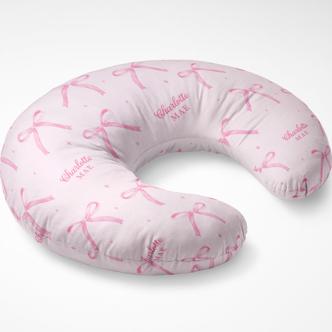 Blush pink nursing pillow cover with watercolor bows, tiny sparkles, and the name Charlotte Mae repeated in pink lettering.