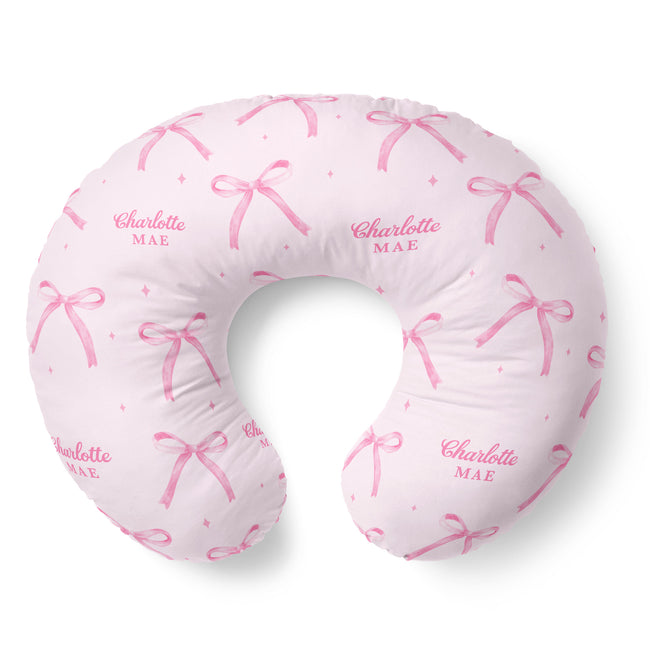 Blush pink nursing pillow cover with watercolor bows, tiny sparkles, and the name Charlotte Mae repeated in pink lettering.