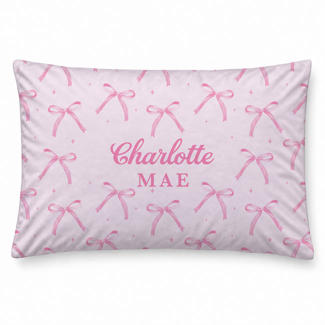 Blush pink pillowcase with watercolor bows and tiny sparkles surrounding the centered name Charlotte Mae in large pink lettering.