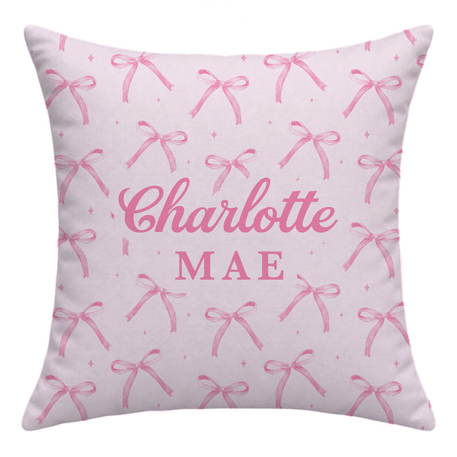 Blush pink throw pillow with watercolor bows and tiny sparkles surrounding the centered name Charlotte Mae in large pink lettering.