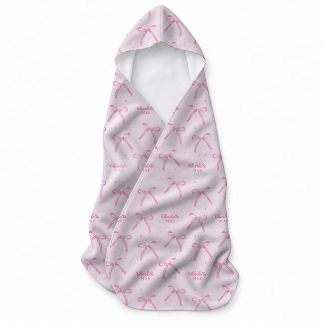 Pale pink hooded towel with pink ribbon bows, tiny sparkle accents, and the name Charlotte Mae repeated throughout.