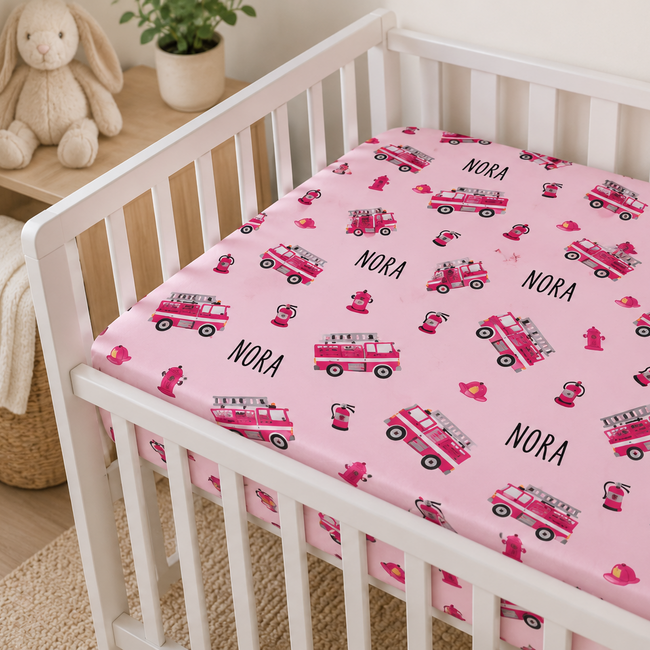 a pink fire trucks personalized crib sheet with the name Nora on it