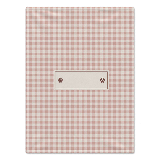 A rectangular pink and white gingham dog blanket featuring a central cream-colored label with two brown paw prints, shown flat against a white background.