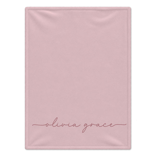A rectangular light pink blanket with the name 'olivia grace' written in a delicate pink cursive script near the bottom, shown flat against a white background.