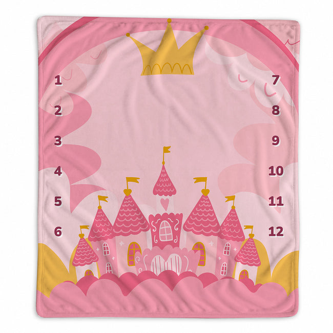A pink baby milestone blanket with a whimsical cartoon castle design, featuring a gold crown at the top and numbers 1 through 12 printed around the outer edge.
