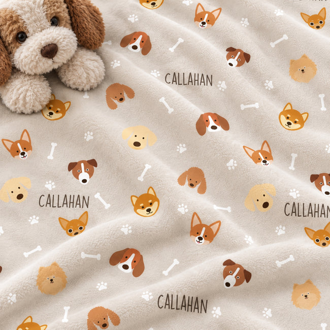 A plush cream-colored blanket with a repeating pattern of cartoon dog faces, bones, paw prints, and the name 'CALLAHAN' in dark brown text. A plush dog toy is partially visible in the top-left corner.