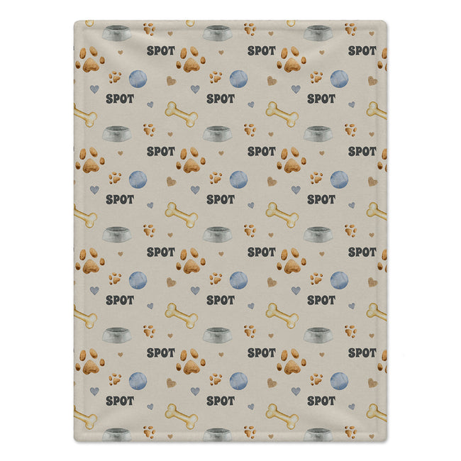 A rectangular dog blanket with a repeating dog-themed pattern featuring the word 'SPOT', paw prints, bones, bowls, and hearts on a light beige background.