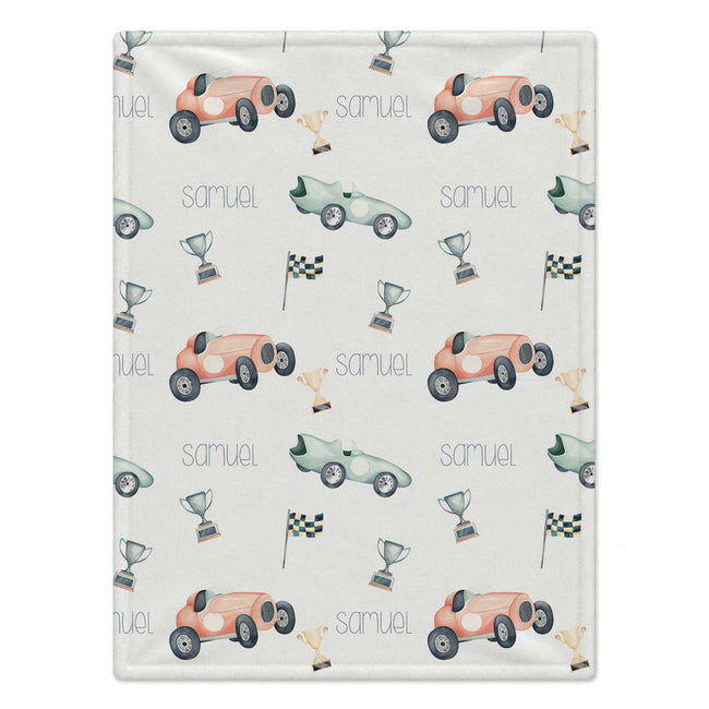 Personalized Race Car Baby Blanket. Vintage-style race cars in coral and mint, trophies, and checkered flags surround a custom name.