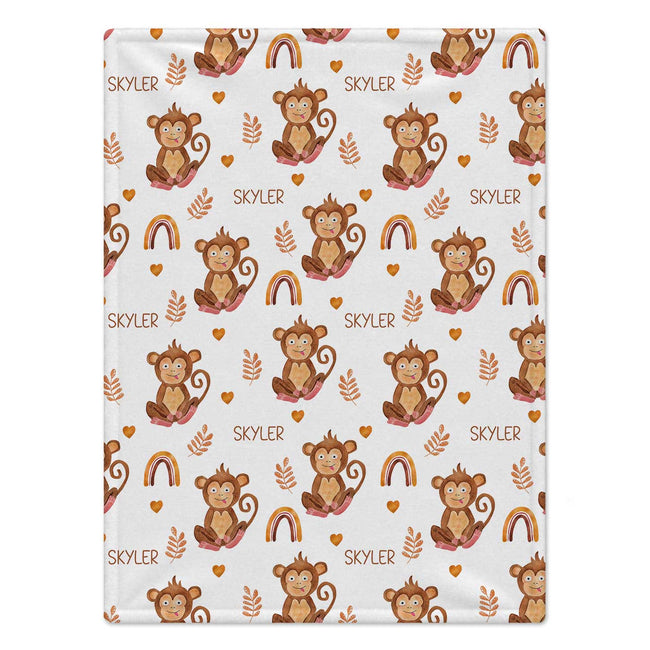 Personalized Monkey and Rainbow Baby Blanket. Cheeky monkeys, warm-colored rainbows, hearts, and leafy sprigs surround a custom name on a white background.