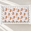 A white crib mattress fitted sheet with a repeating pattern of brown cartoon monkeys, rainbows, leaves, and the word 'SKYLER', shown inside a white crib on a light textured floor.