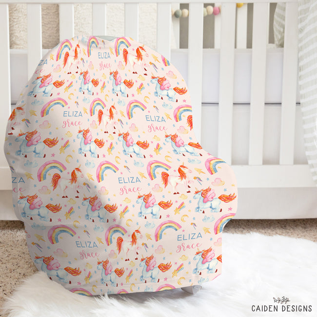 A baby car seat cover with a whimsical unicorn and rainbow pattern, personalized with the names 'Eliza Grace', shown on a white baby car seat in a nursery setting.