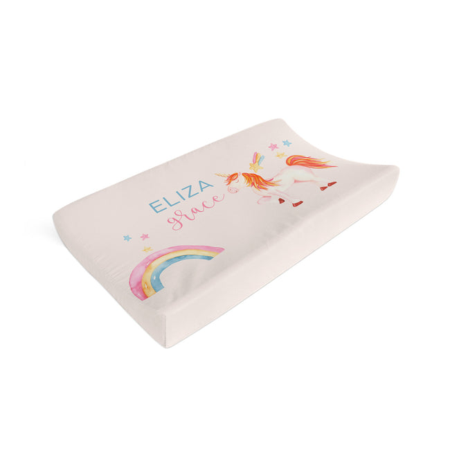 A contoured baby support pillow with a custom printed design. The pillow features a light beige fabric cover decorated with a colorful rainbow, a whimsical unicorn, and the personalized name 'ELIZA Grace' in blue and pink text.