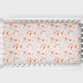 A crib mattress fitted sheet with a whimsical unicorn and rainbow pattern, shown inside a white wooden crib. The sheet features a light pink background with orange, pink, and blue unicorns, pastel rainbow arches, and the text 'ELIZA grace' repeated throughout.