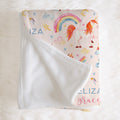 A personalized baby blanket with a white sherpa backing and a printed front featuring a unicorn, rainbow, stars, and clouds on a light pink background. The name 'ELIZABETH' is printed in blue and pink lettering.