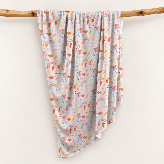 Personalized swaddle blanket hanging on a wooden rail with watercolor unicorns, rainbows, stars and custom name Eliza Grace.
