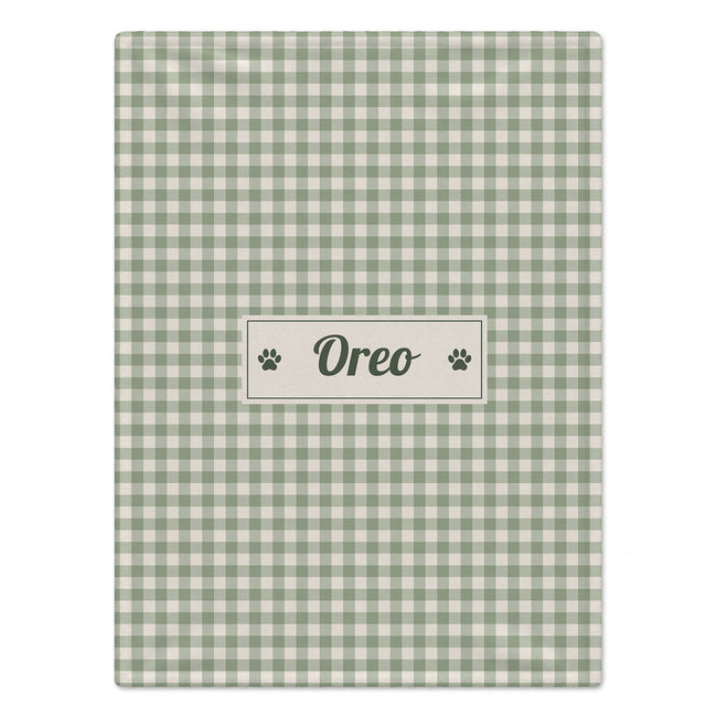 A rectangular pet blanket with a sage green and cream gingham checkered pattern, featuring a central cream label with the name 'Oreo' and paw prints.
