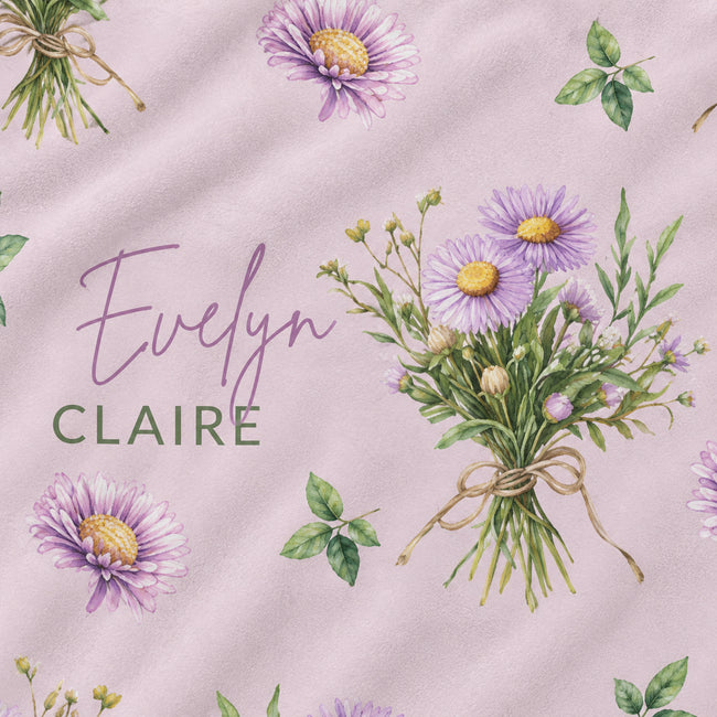 A close-up of a fabric or wallpaper pattern featuring purple and yellow aster flowers, green leaves, and a bouquet tied with a ribbon on a soft pink background. The text 'Evelyn CLAIRE' is printed across the design.