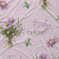 Mauve-pink fabric with lavender aster bouquets, yellow flower centers, green leaves, and the name Evelyn Claire.