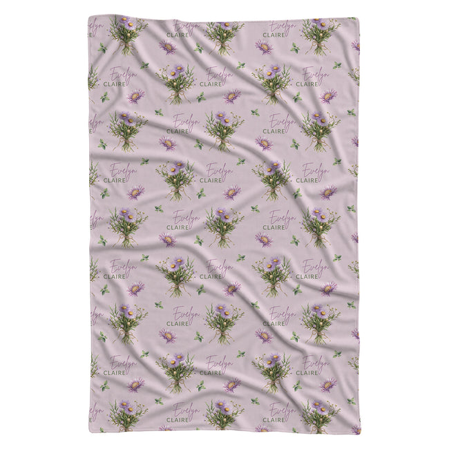 Mauve-pink swaddle blanket with lavender aster bouquets, golden centers, green leaves, and the name Evelyn Claire.