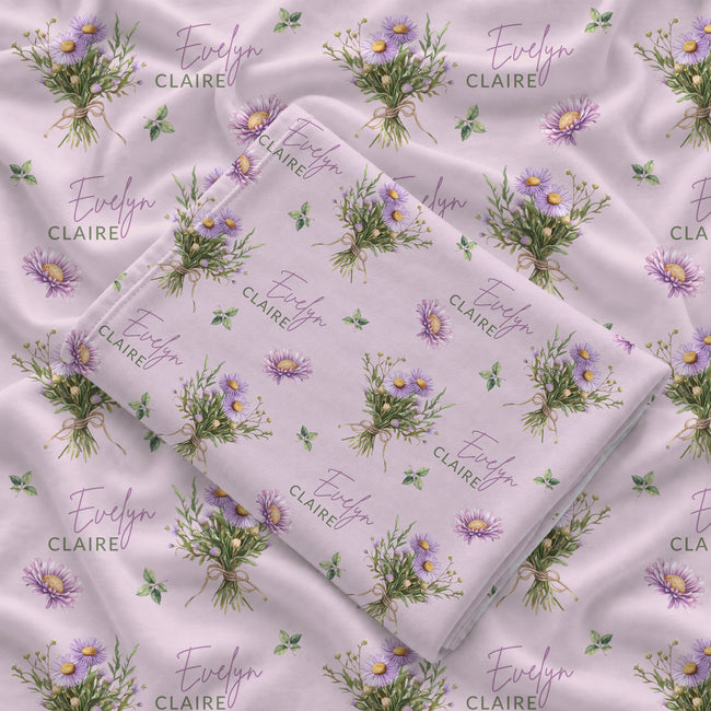 Mauve-pink swaddle blanket with lavender aster bouquets, golden centers, green leaves, and the name Evelyn Claire.